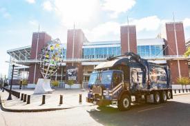 A blue garbage truck parked outside of Reser Football stadium on a sunny day with white clouds in the sky.