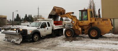 Yellow bucket loader putting sand in the back of a pickup truck.